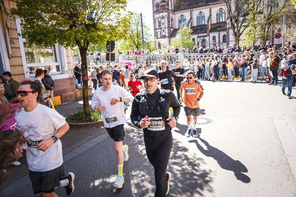 Mehrere Läufer in einer Kurve. Links und rechts feuern Zuschauer die Läufer an.